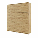 Closed space-saving vertical wall bed in natural oak artisan wood finish, seamlessly blending into bedroom decor as a tall cupboard